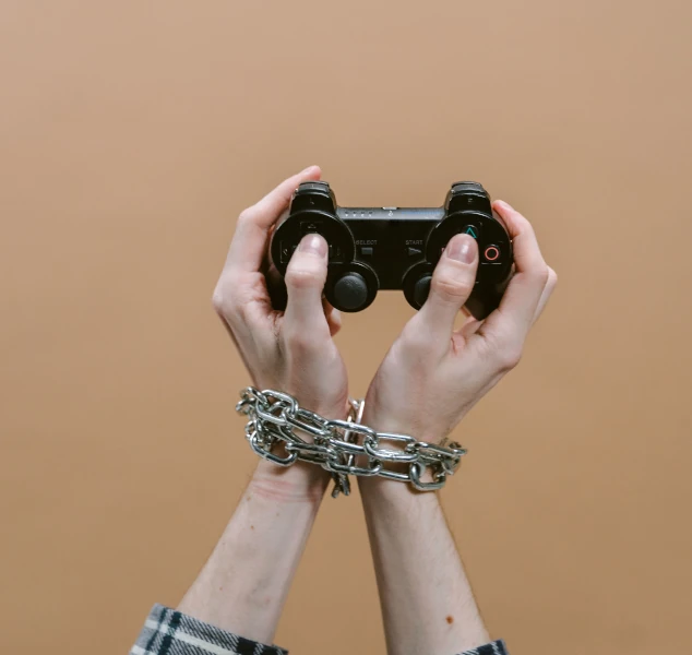Adolescent jouant aux jeux vidéo avec des chaînes aux poignets symbolisant la difficulté à arrêter et la perte de contrôle